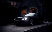 Черный Bentley Continental GT темным вечером у парадного входа в коттедж